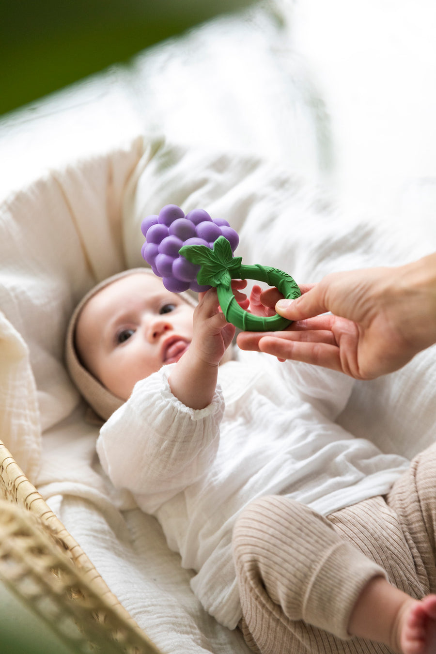 A baby reaching for an Oli & Carol Grape Rattle Teether