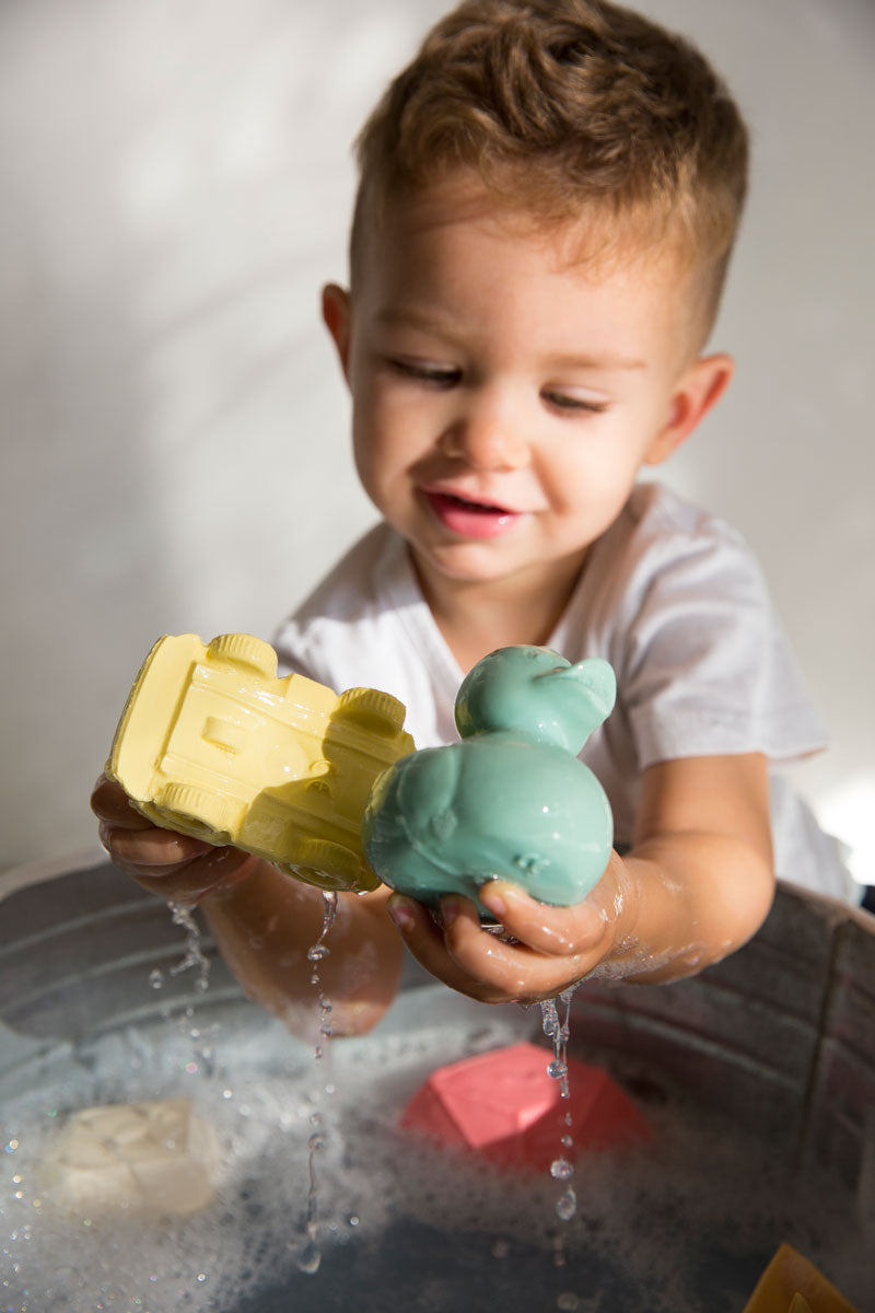 Child holding onto oli and carol yellow car and mint duck above a tub of water