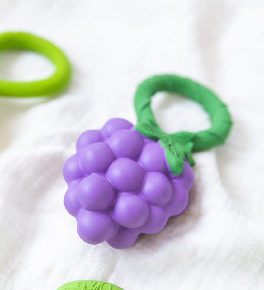 Oli & Carol Grape Rattle Teether pictured on a white muslin cloth