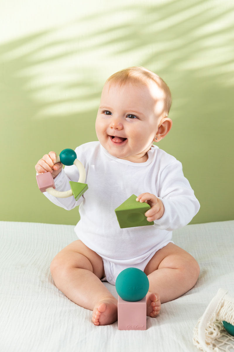 Baby holding the Oli & Carol X Bauhaus Movement Teething Ring in Pastel Colours and playing with the pastel geometric blocks