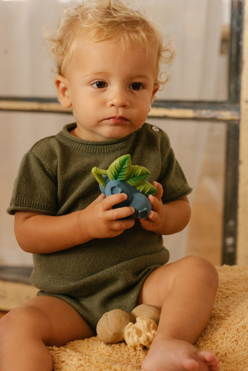 Close up of a child holding the oli and carol natural rubber baby teething toys on a cream blanket