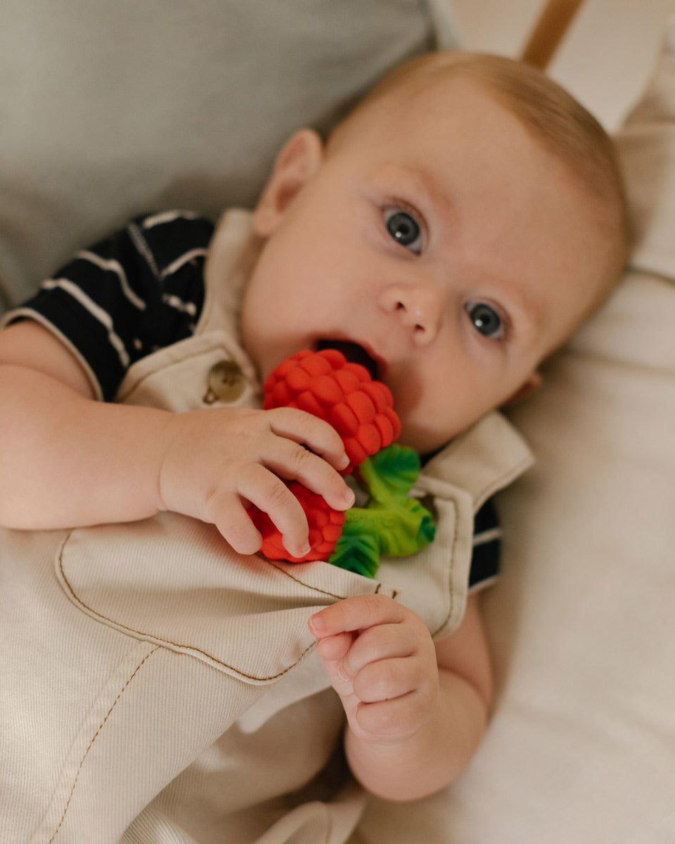 Close up of a toddler chewing on the oli and carol natural rubber raspberry teething toy