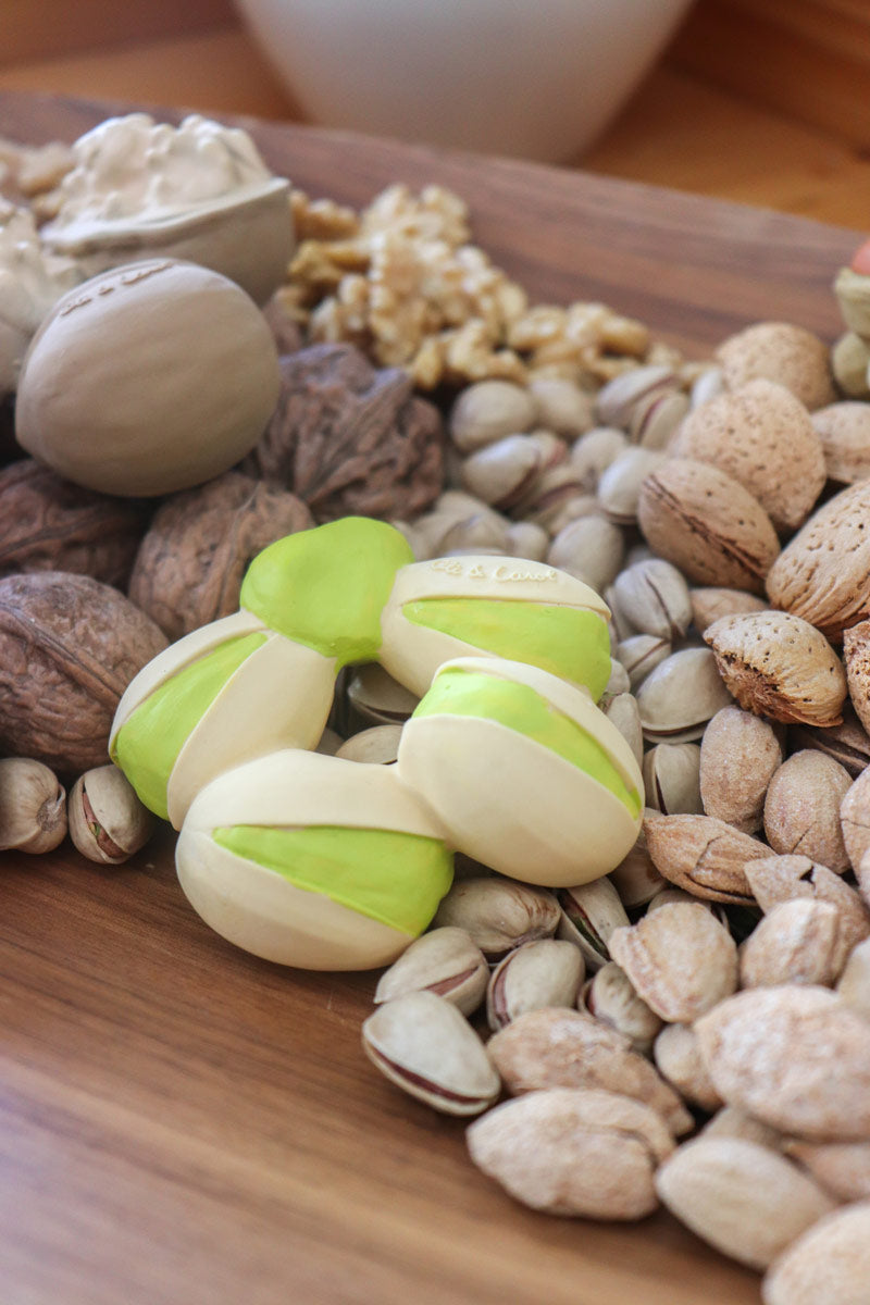 Oli and carol natural rubber pistachio toy on a wooden table next to a pile of nuts