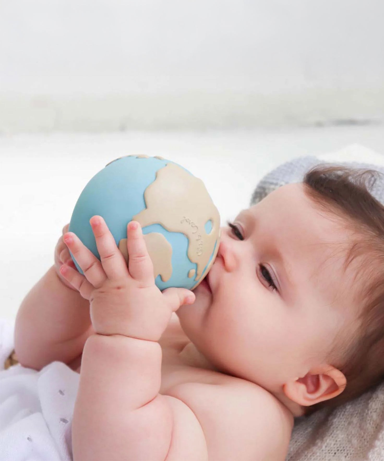 A baby holding the Oli &amp; Carol Earthy The World Ball in their hands.