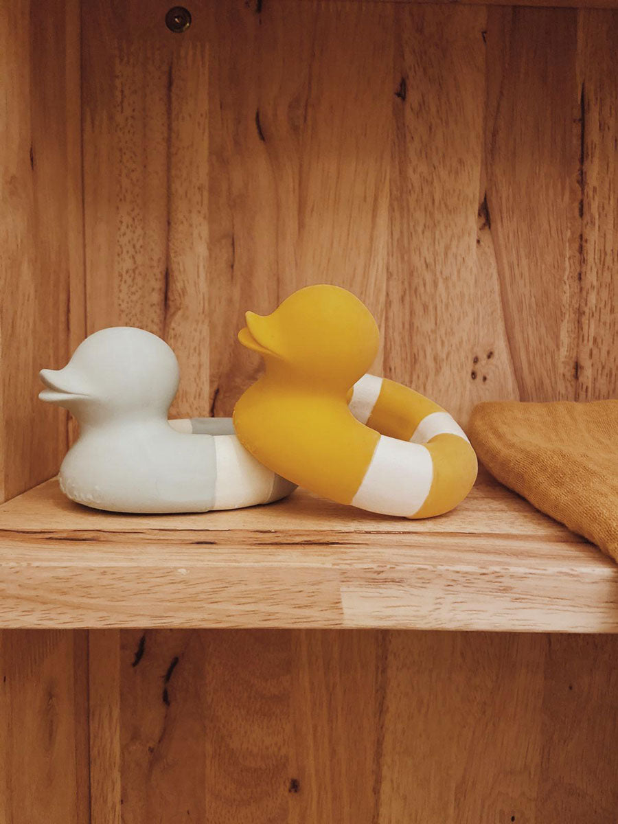 Yellow and mint coloured Oli & Carol Flo The Floatie Ducks placed on a wooden shelving unit