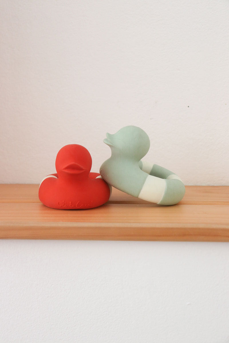 One Red and one mint coloured Oli & Carol Flo The Floatie ducks placed on a wooden shelf