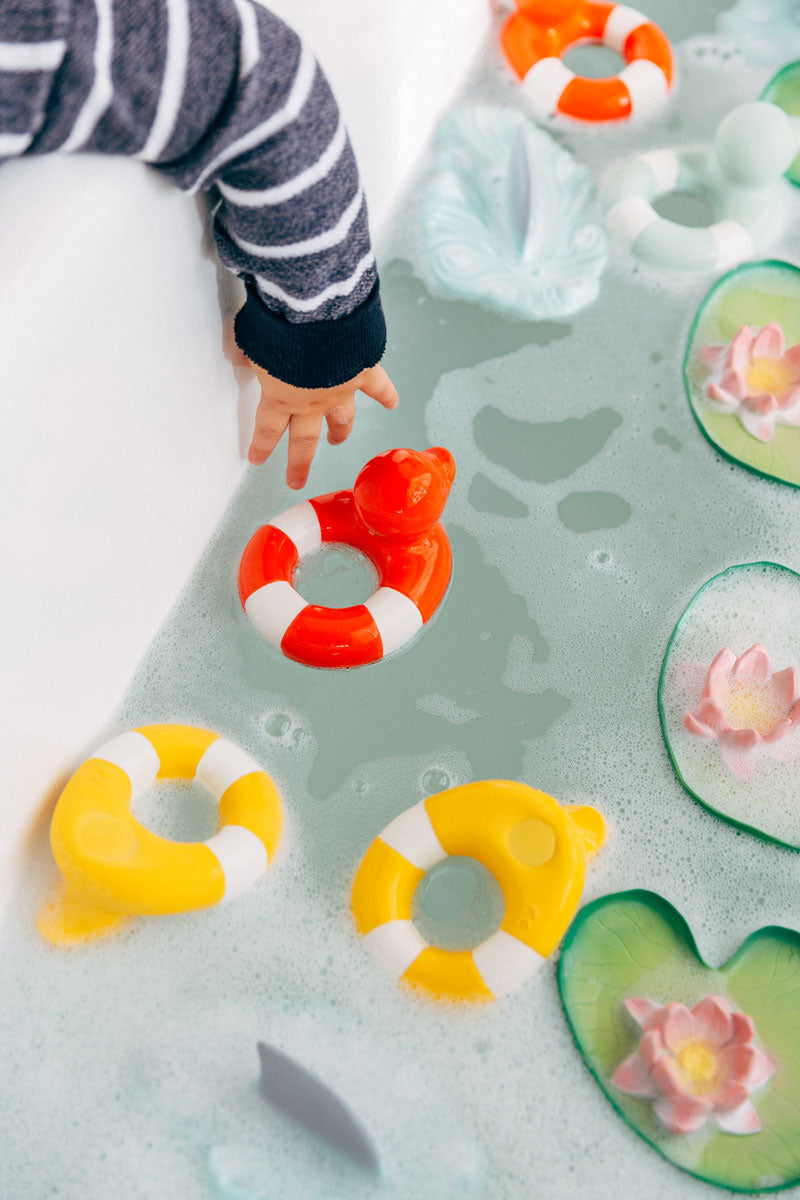 Child's hand reaching into a bath for the Oli & Carol Flo The Floatie Duck Red