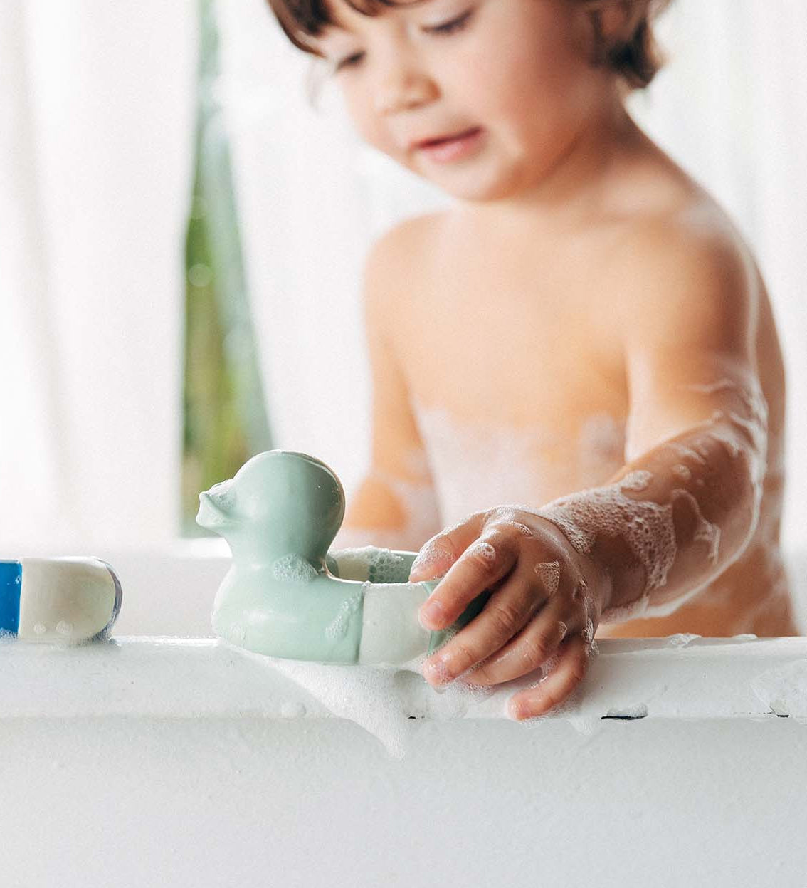 A child playing with the Oli & Carol Flo The Floatie Duck Mint in the bath. 