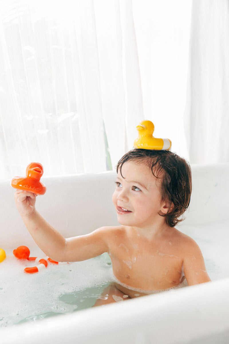 Child holding a red Oli & Carol Flo The Floatie Duck in hand with a yellow one balanced on their head