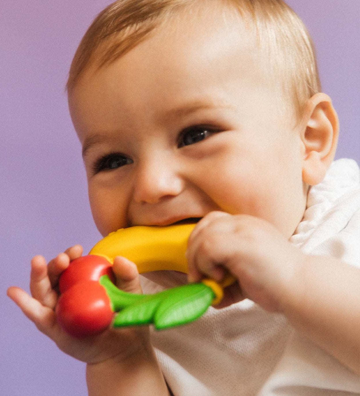 A baby chewing on the Oli & Carol Natural Rubber Fruit Teething Ring.