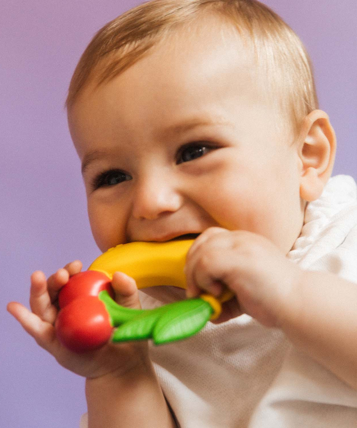 A baby chewing on the Oli & Carol Natural Rubber Fruit Teething Ring.