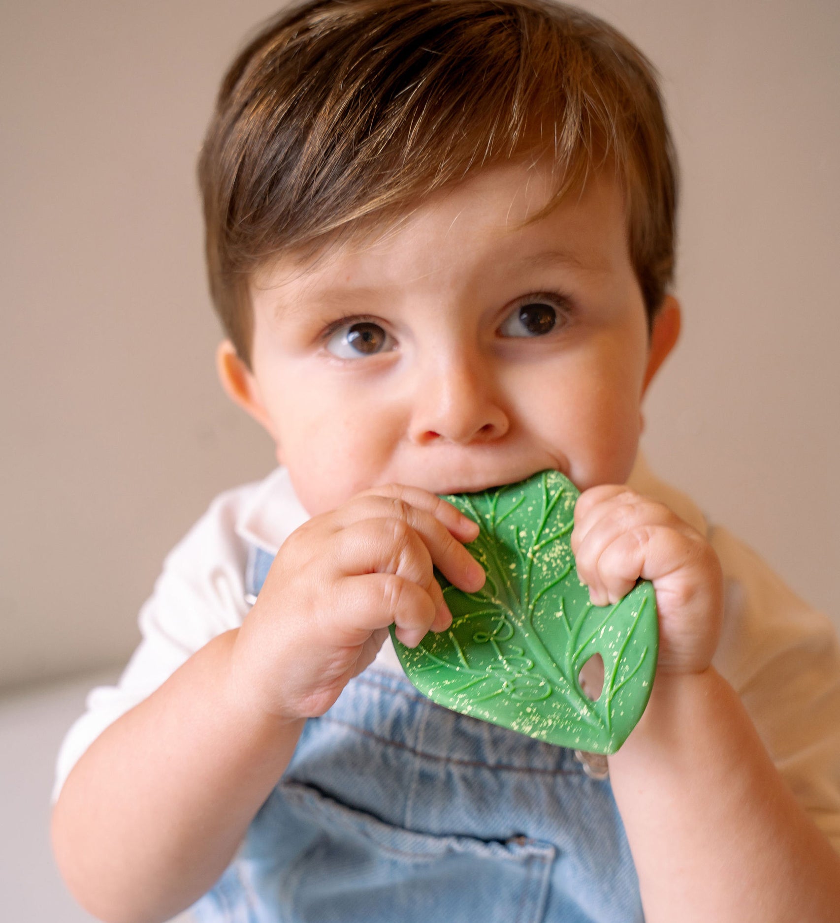 A baby holding the Oli & Carol Chlorophyll Leaf Baby Teether in their hands while chewing on it.