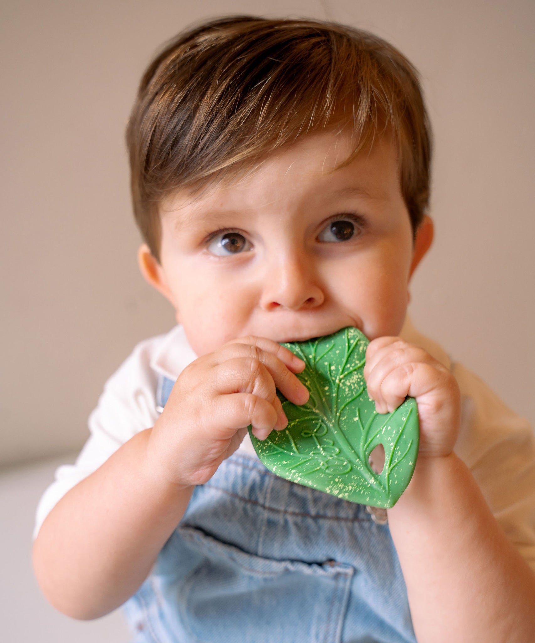 A baby holding the Oli & Carol Chlorophyll Leaf Baby Teether in their hands while chewing on it.