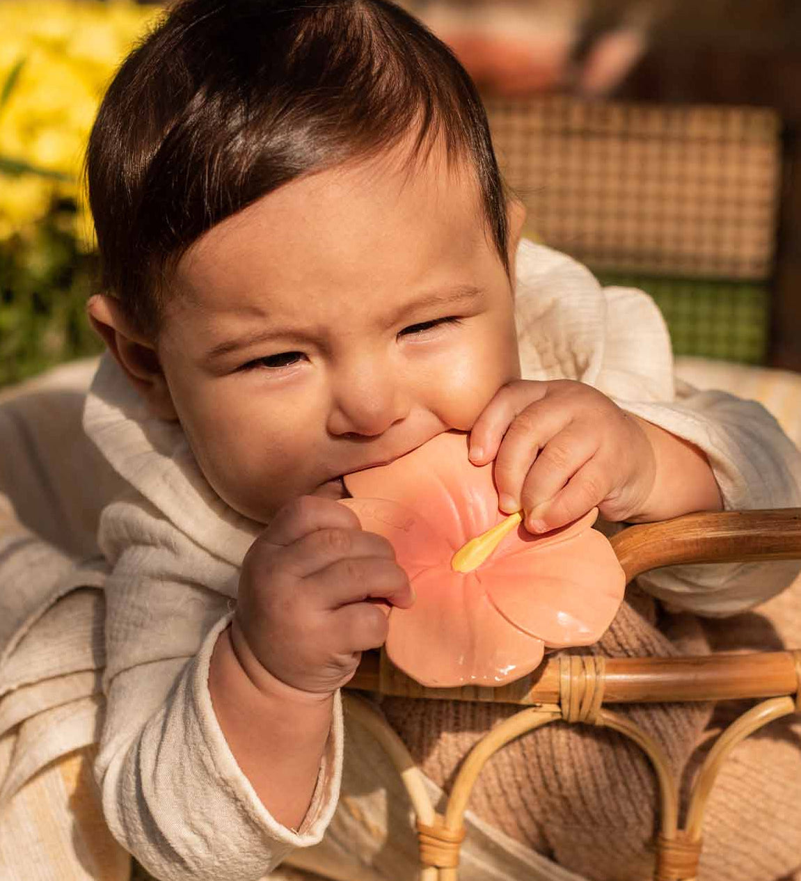 A baby holding and chewing on the Oli & Carol Iris The Hibiscus Baby Teether