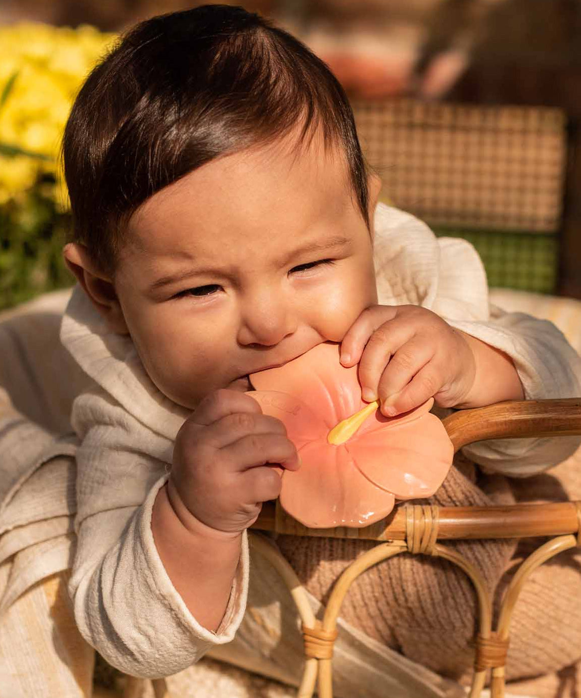 A baby holding and chewing on the Oli & Carol Iris The Hibiscus Baby Teether