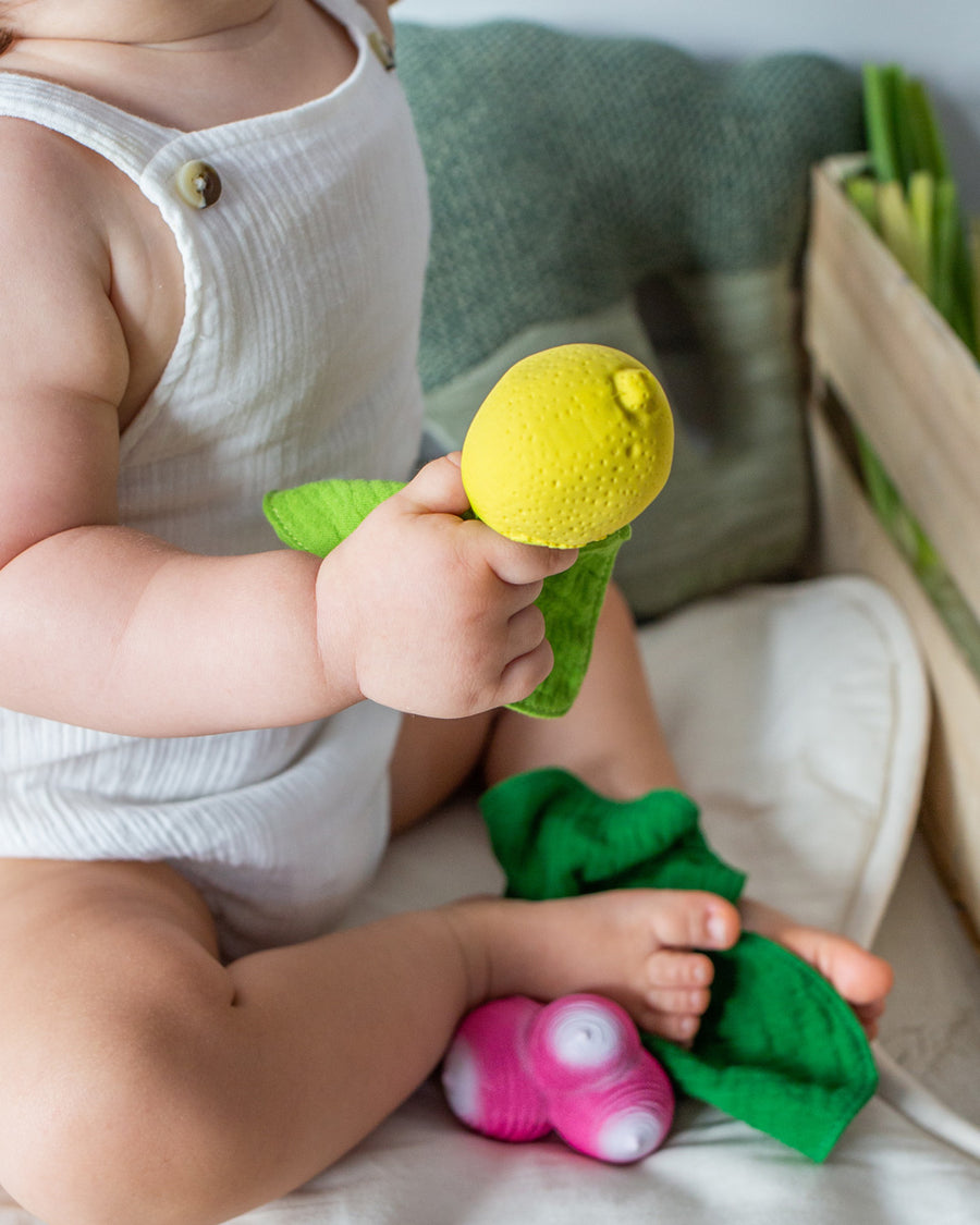 Close up of a young child holding the Oli & Carol soft mini lemon baby teething and comforter toy