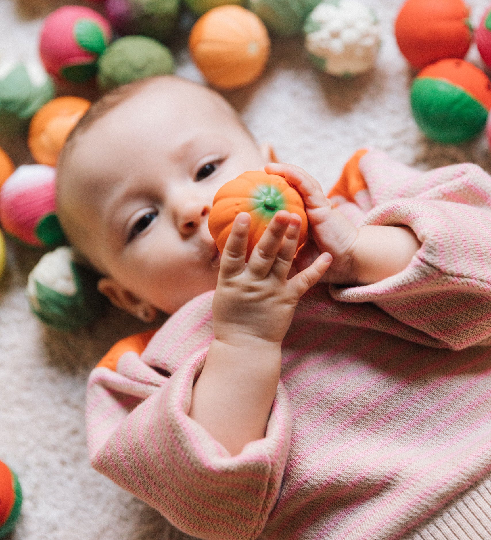 A baby grasping onto the pumpkin ball from the Oli & Carol Vegetable soup Baby Sensory Balls set