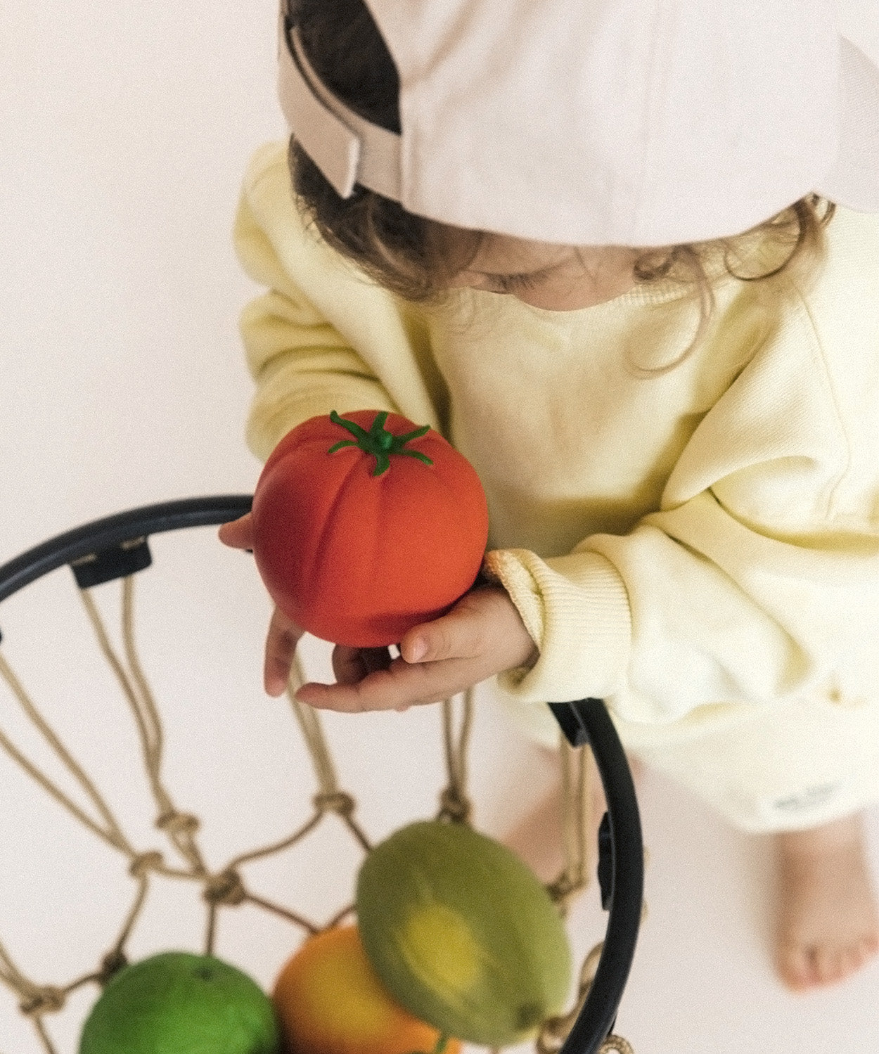 Child putting the Tomato Oli & Carol 100% Natural Rubber Baby Sensory Ball into a basketball hoop