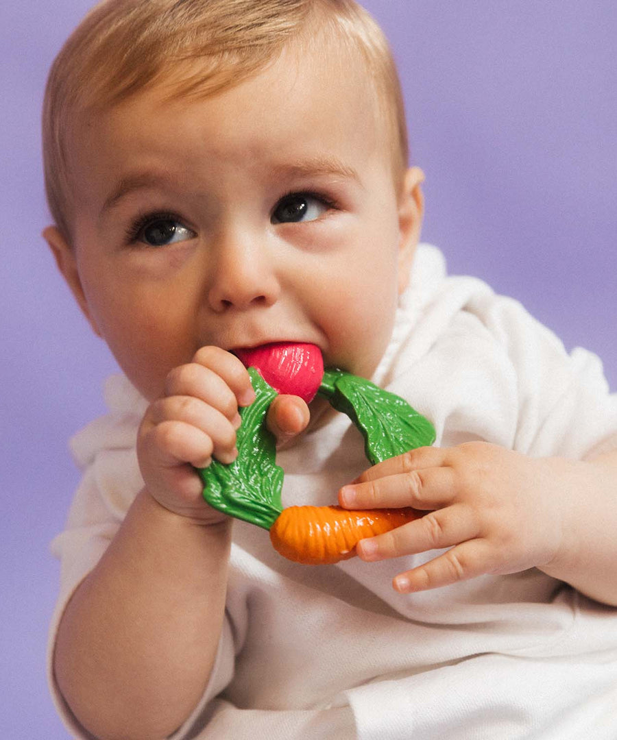 A baby clutching the Oli & Carol Natural Rubber Veggie Teething Ring.