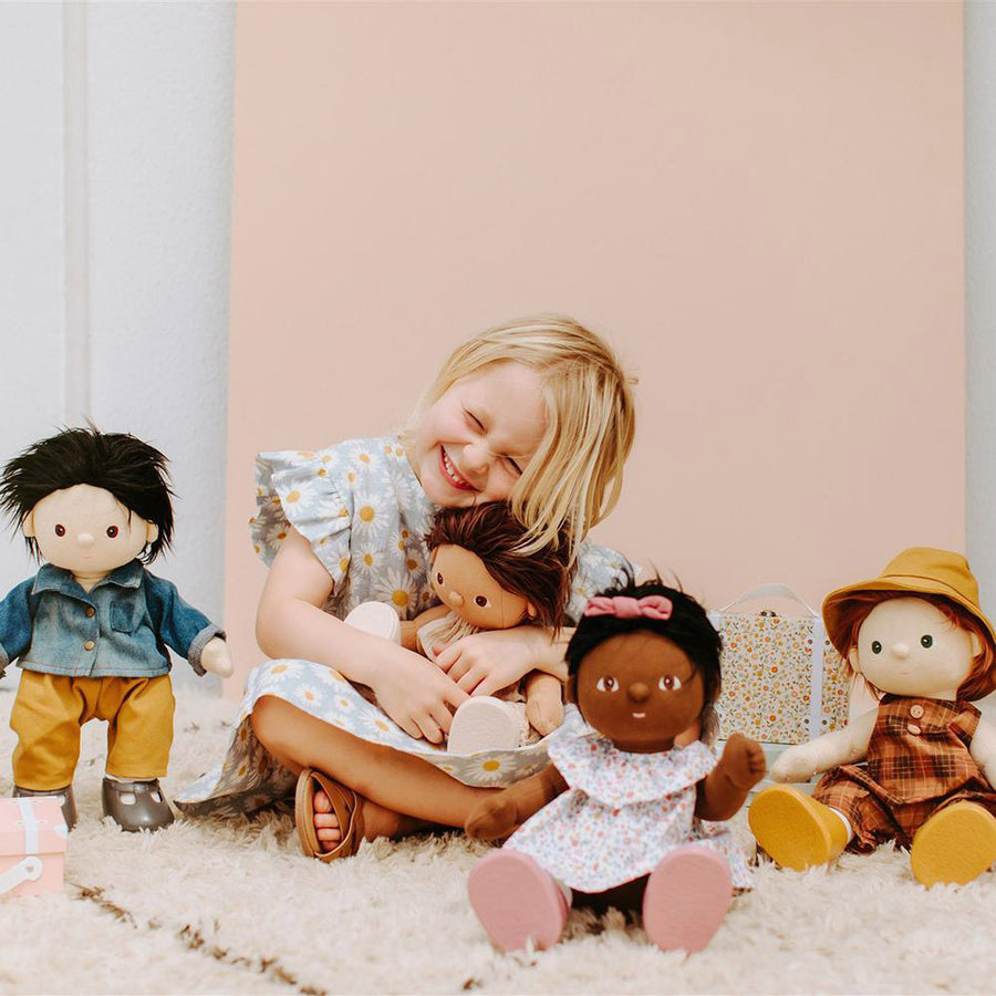 Little girl sat in a pink room surrounded by Olli ella dinkum dolls wearing the travel tog dress up outfits