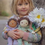 A child holding two Olli Ella Bunny Dinky Dinkum Dolls in their arms, Babs the purple bunny and  Biscuit the mint green bunny. 