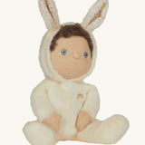 Olli Ella cream coloured Basil Bunny Dinky Dinkum Doll in a seated position with the bunny ear hood up showing the dinky dolls brown coloured curly hair peeping out at the  front