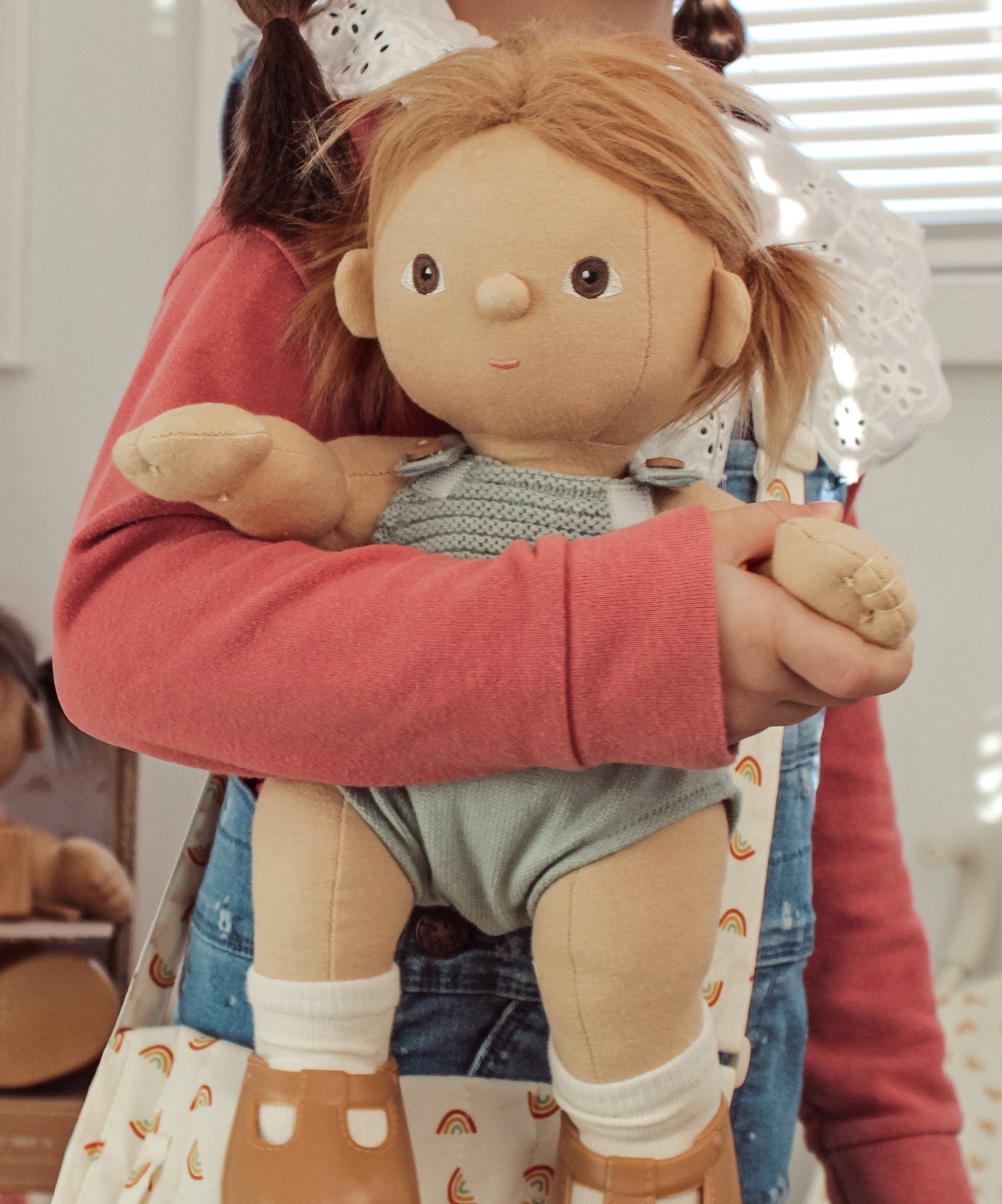 A close up of a child holding an Olli Ella Gigi Dinkum doll.