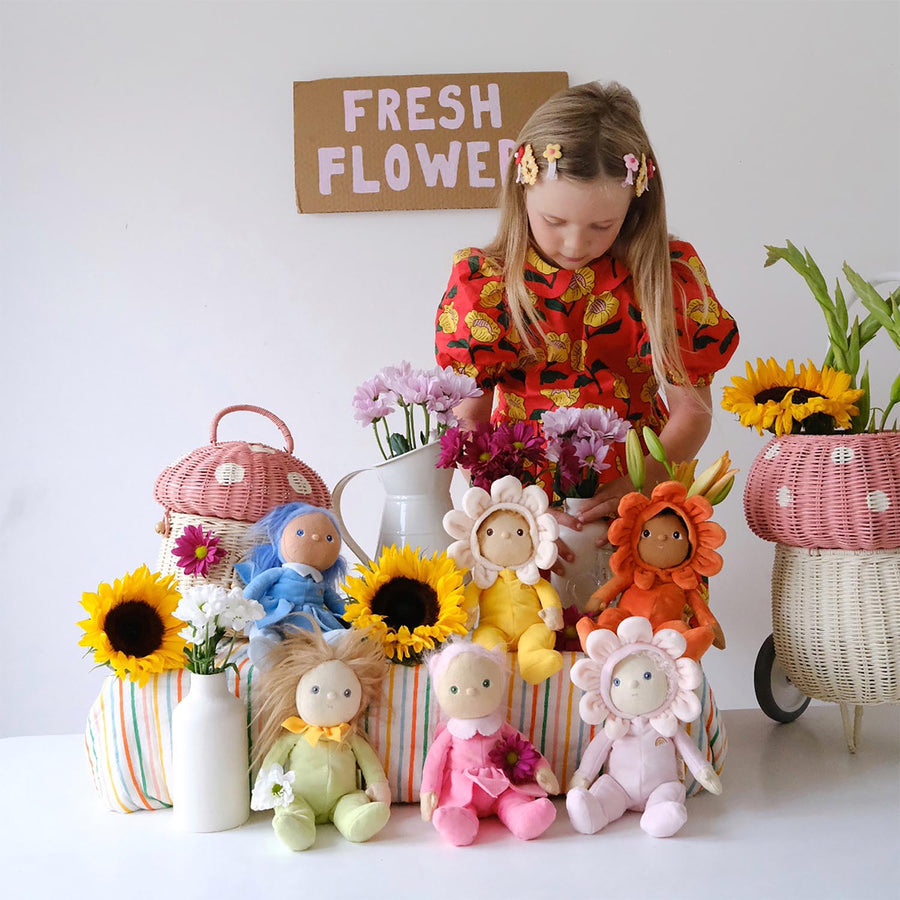 Olli Ella Dinky Dinkum Blossom Buds - Lily sat on a wooden bench surrounded by the rest of the blossom bud range with a child holding Sunflower doll in the foreground