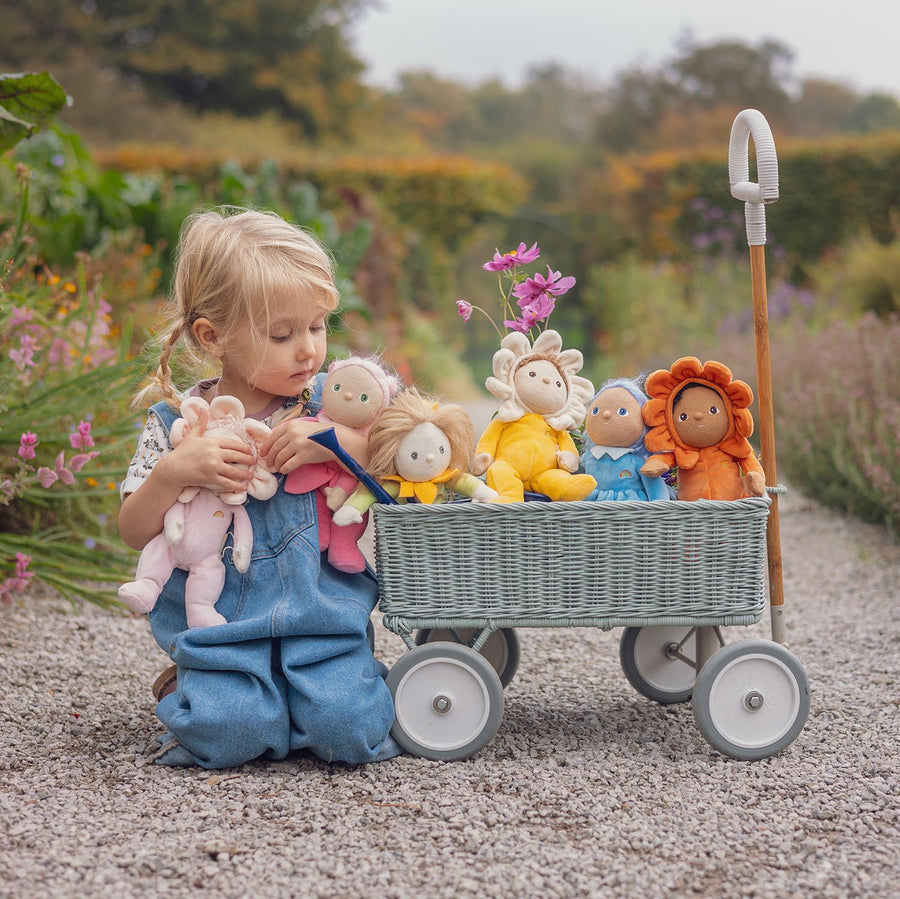 Olli Ella Dinky Dinkum Blossom Buds  Rose sat on a wooden bench surrounded by the rest of the blossom bud range with a child holding Sunflower doll in the foreground