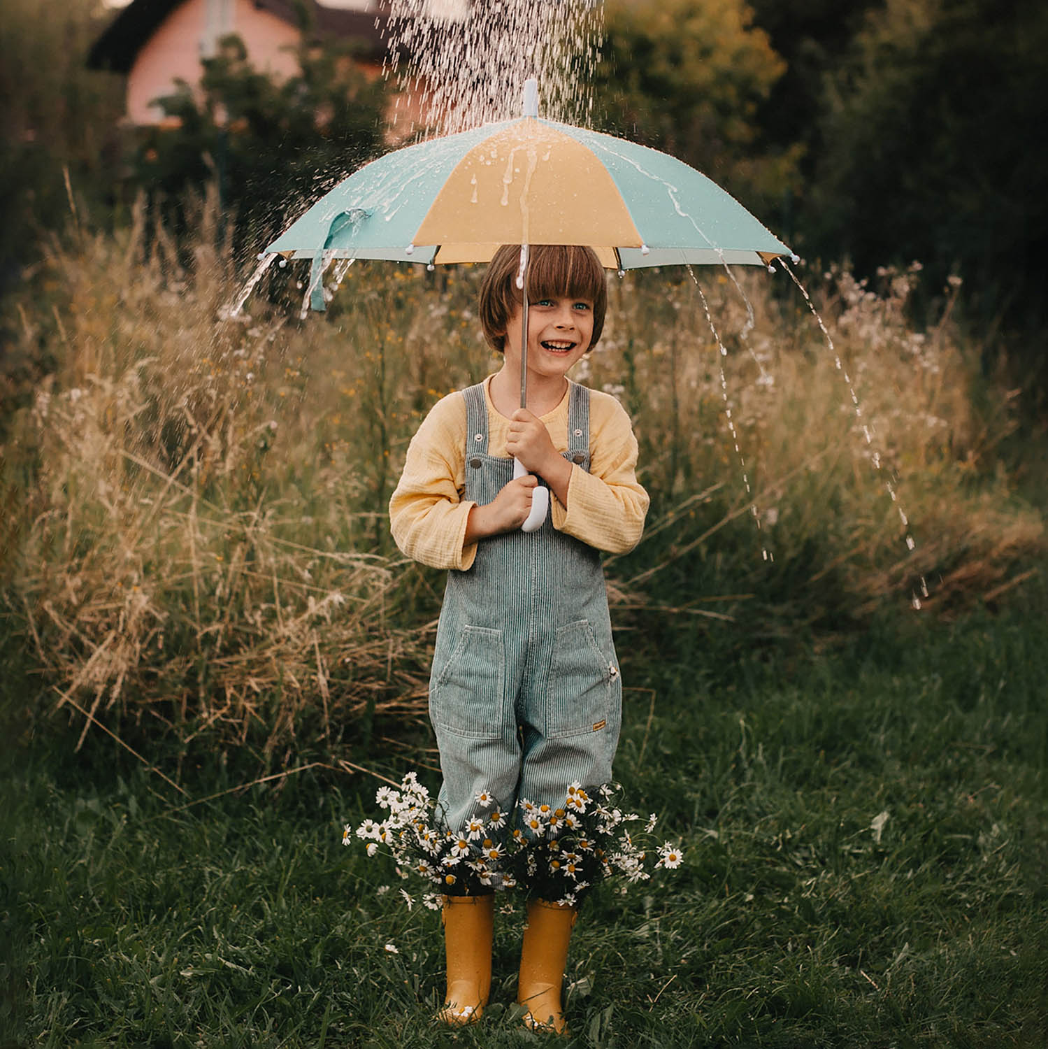 Olli Ella See-Ya Umbrella - Blue Butter. Yellow and Blue coloured umbrella being held by with rain dropping over the umbrella