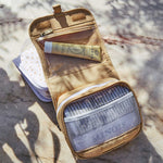 The Olli Ella butterscotch See-Ya Wash Bag placed on a marble surface open with toiletries inside