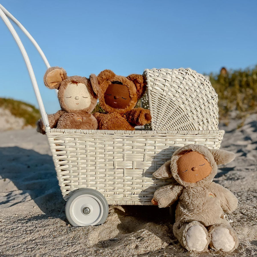 Close up of the Olli Ella kids hand-woven rattan strolley in the chalk colour on the beach