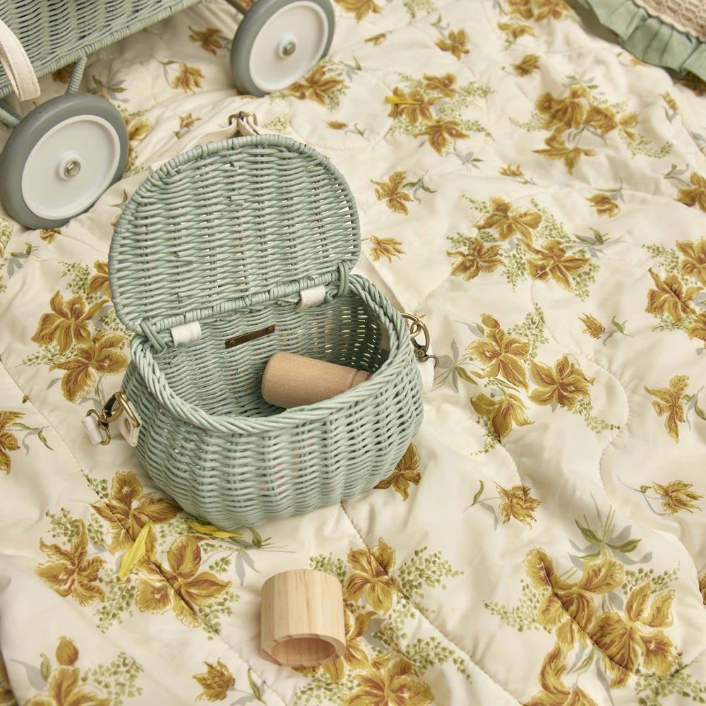 Olli ella childrens blue rattan chari bag on a floral duvet with some wooden blocks inside