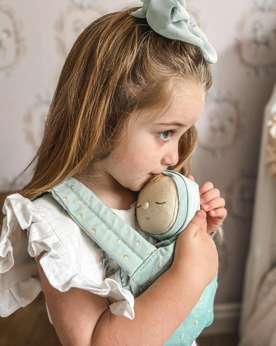 Close up of a young girl hugging a dozy dinkum doll in the Olli Ella boat print baby carrier