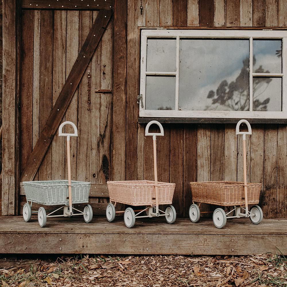 3 Olli Ella rattan wonder wagon toys lined up in front of a wooden house