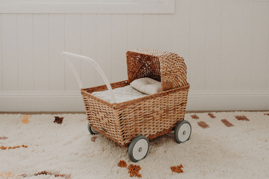 Olli ella natural rattan strolley toy with the seafoam bedding set inside on a white carpet