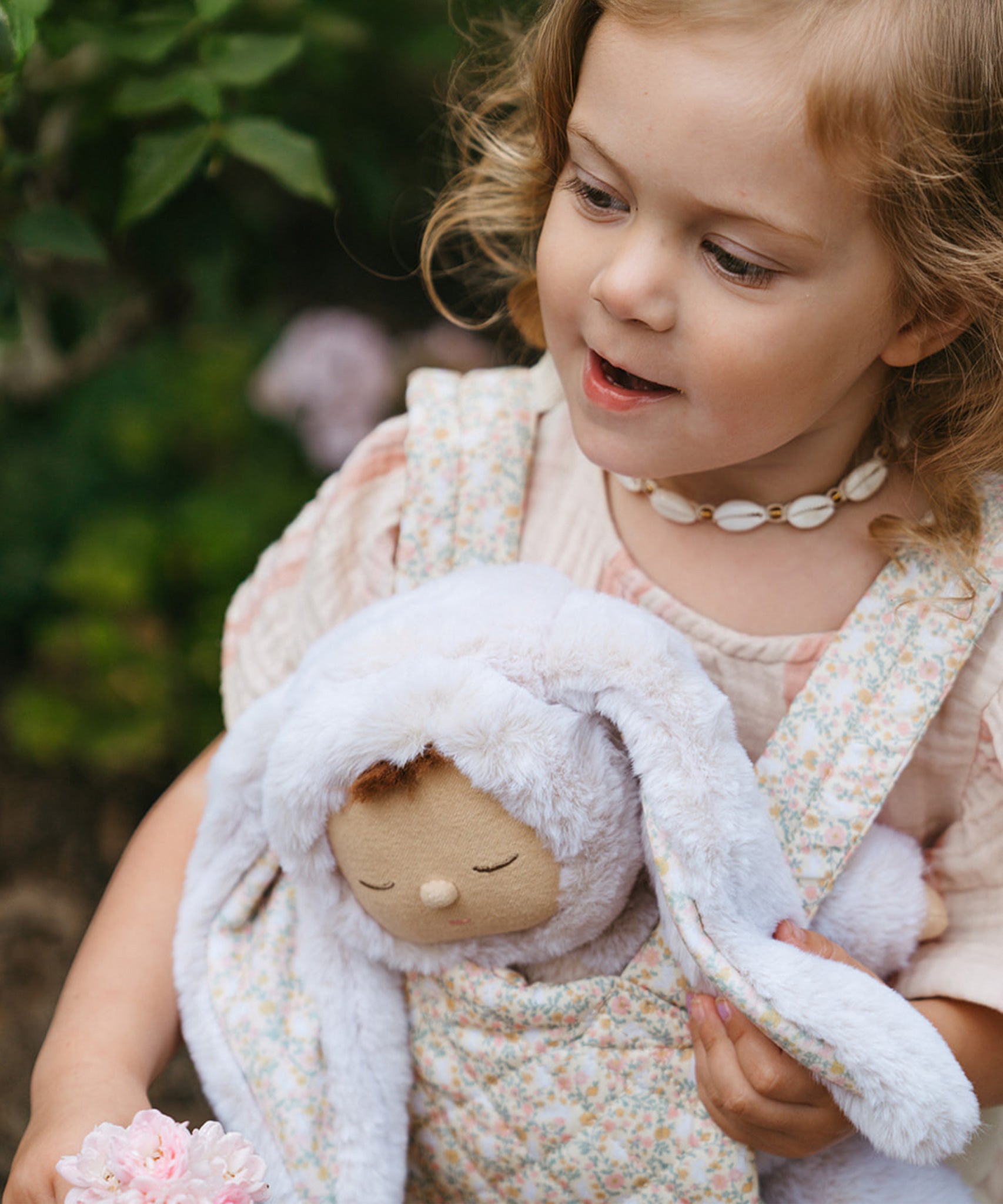 A close up of a child carrying the Olli Ella Bunny Lala Cozy Dinkum in a Olli Ella toy carrier. 