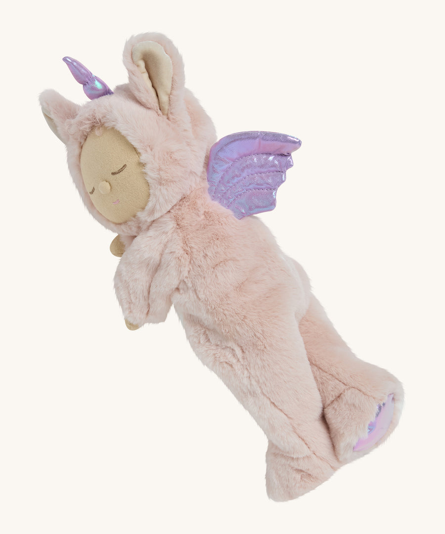 A pink fluffy Olli Ella unicorn doll lying on it's side on a cream background