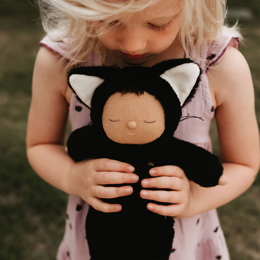 Olli Ella Cozy Dinkums - Black Cat Nox is held in the hands of a young child.