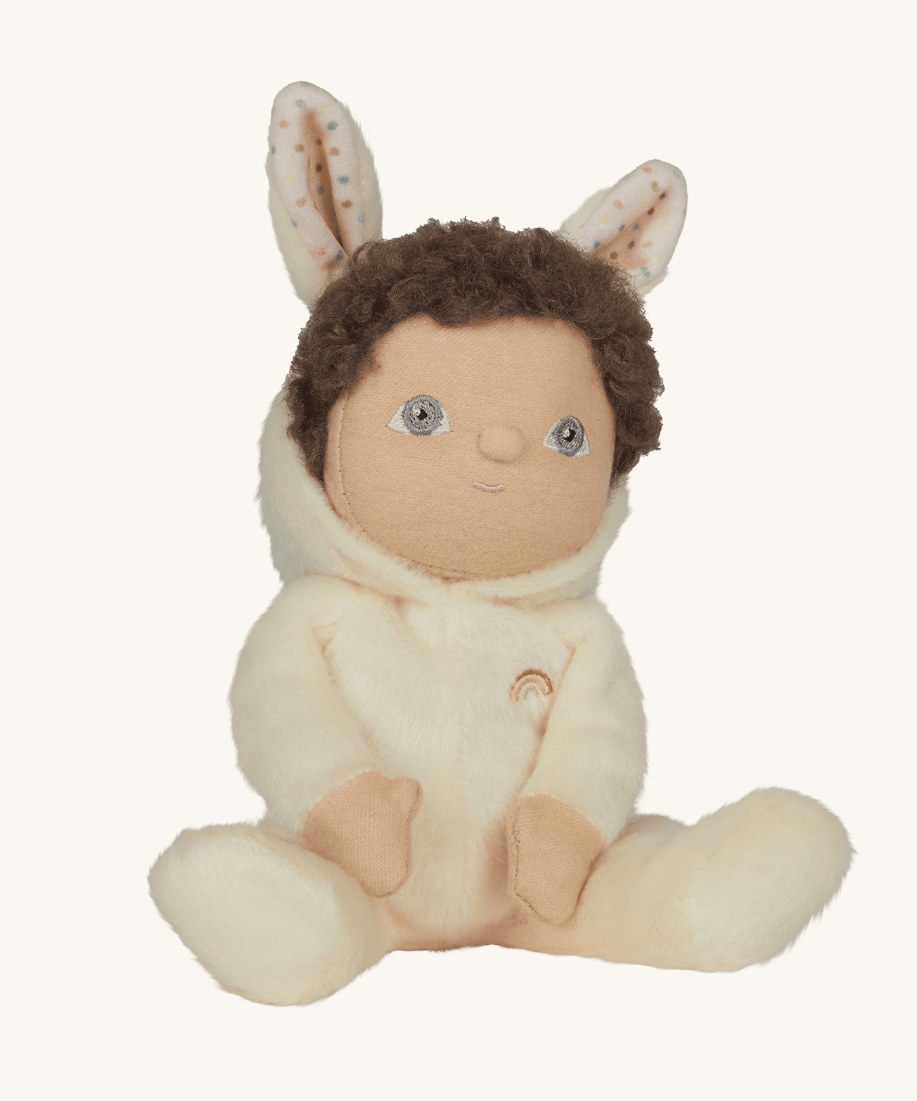 Olli Ella cream coloured Basil Bunny Dinky Dinkum Doll in a seated position with the bunny ear hood pulled down slightly, showing the dinky dolls brown coloured curly hair