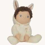 Olli Ella cream coloured Basil Bunny Dinky Dinkum Doll in a seated position with the bunny ear hood pulled down slightly, showing the dinky dolls brown coloured curly hair