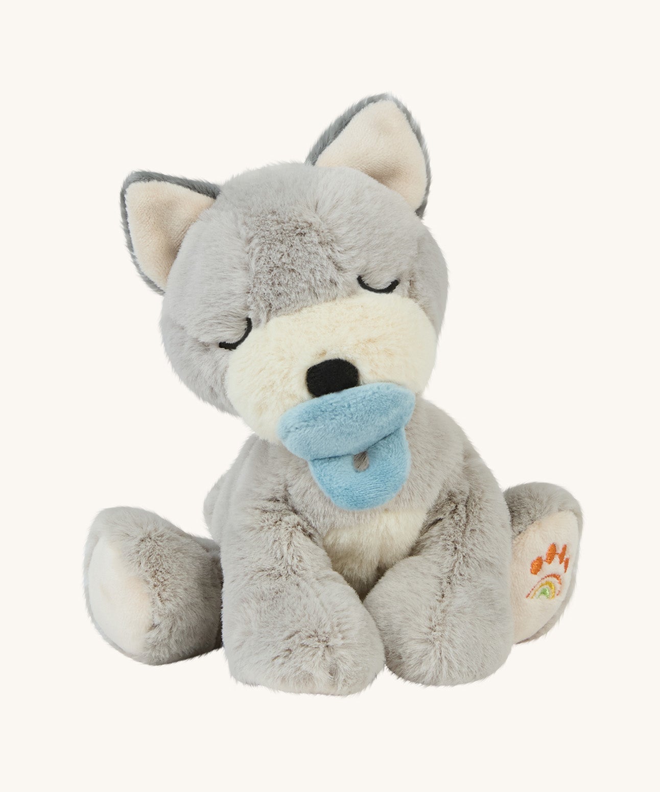 A soft grey sitting Olli Ella dinkum puppy with a magnetic dog toy on its mouth on a cream background.