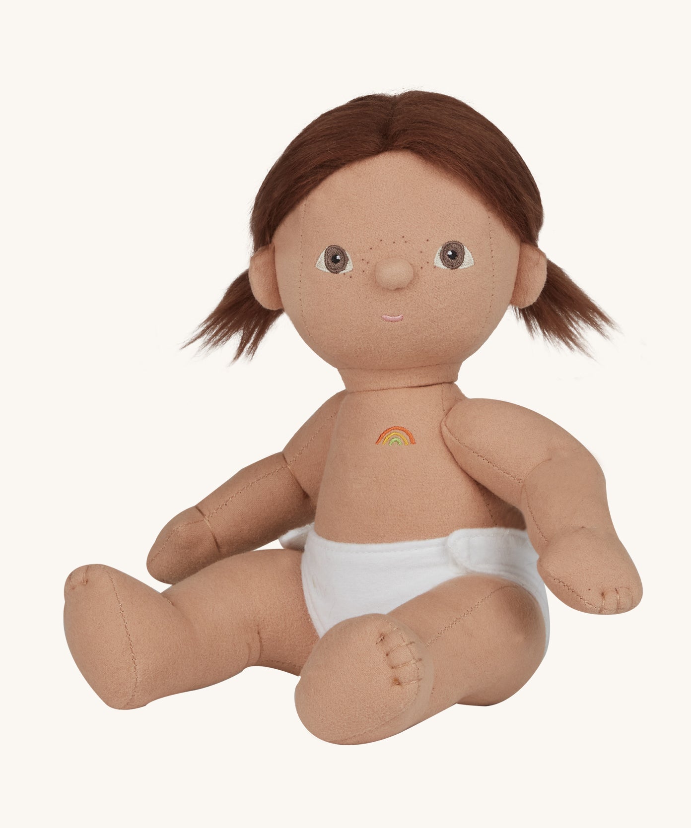 An Olli Ella Dottie Dinkum Doll on a plain background. The doll has brown hair and brown eyes. The hair is in pig tails and the doll is a seated position with just the nappy on. 