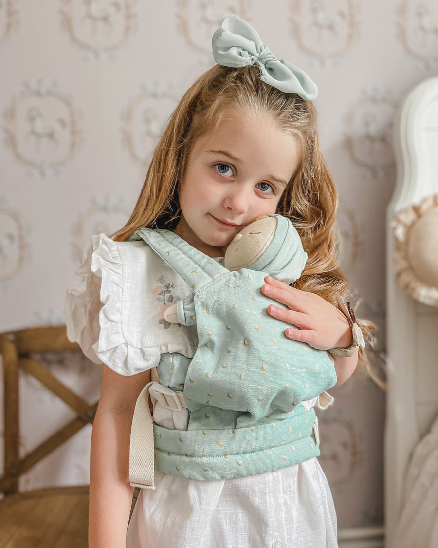 Young girl stood wearing the Olli Ella dozy dinkum doll carrier in the ocean boats print