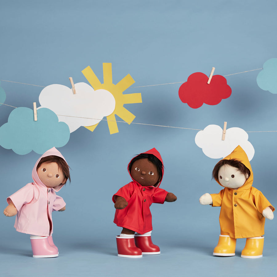 3 olli ella dinkum doll toys stood on a blue background wearing the dress up rainy day outfits in red