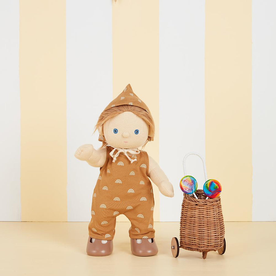 Olli Ella dinkum doll stood on a cream and white striped background wearing the Rolo Romper set next to a brown wooden basket