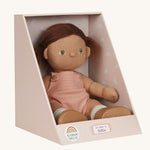 An Olli Ella Dottie Dinkum Doll on a plain background shown in a seated position in it's box. The doll has brown hair and brown eyes. The hair is in pig tails and the doll is a seated position with just the nappy on. 