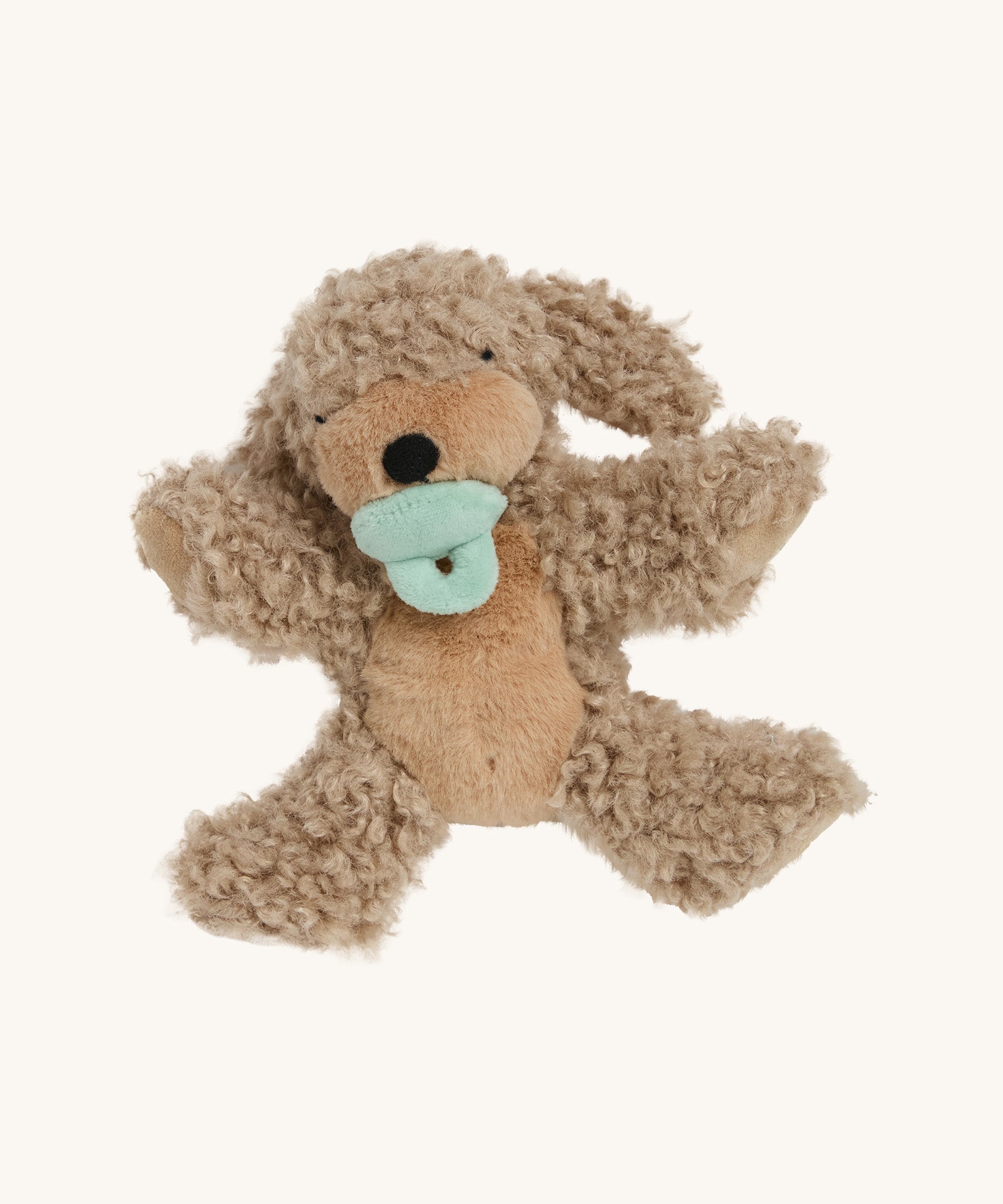 A soft and fluffy Brown Olli Ella Benny puppy with a magnetic dog toy in its mouth on a cream background.