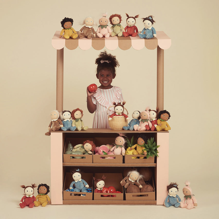 Young girl stood under a role play market stall surrounded by Olli Ella dinky doll toys