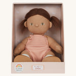 An Olli Ella Dottie Dinkum Doll on a plain background shown in a seated position in it's box. The doll has brown hair and brown eyes. The hair is in pig tails and the doll is a seated position with just the nappy on. 